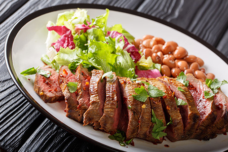 Grilled sliced carne asada beef steak with lettuce and beans close-up on a plate. horizontal
