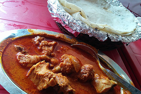 Steel dish with Chicken Curry. Roti in foil behind bowl