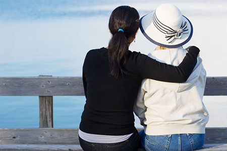 Closeup of mother and mature daughter siting on wooden bench while looking at the lake