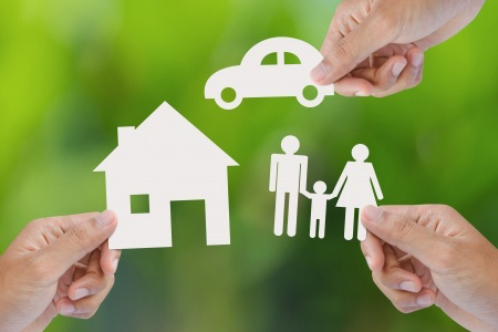 Hand holding a paper home, car, family on green background