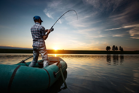 Mature man fishing from the boat on the pond at sunset