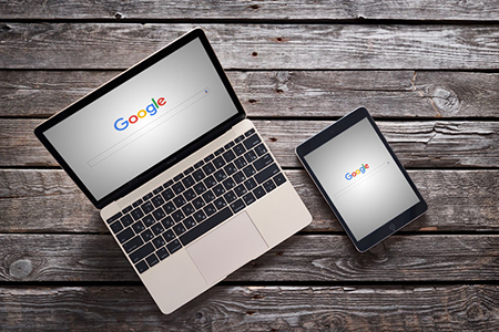 Laptop and tablet on wooden planks. Google search landing page displayed