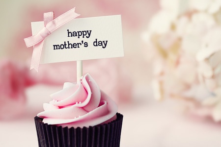 Cupcake with pink frosting and Happy Mothers Day message with pink bow. Blurred background