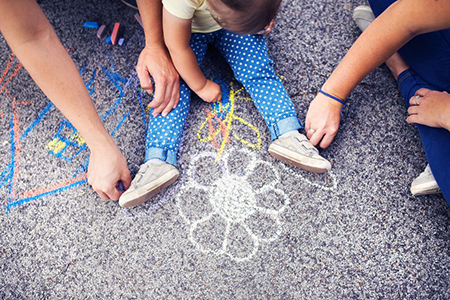 Close up of little girl and her parents drawing with chalks on the sidewalk