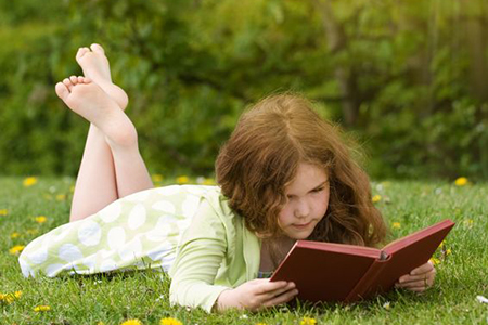 Young girl reading a book outdoors in summertime