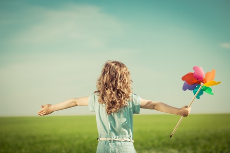 young girl holding colorful wind fan with arms open - from behind - standing in large open field
