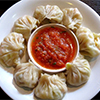 chicken momo dumplings on white plate with red sauce in centre