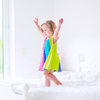 Toddler girl in a colorful dress jumping on a big white bed laughing