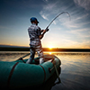 Mature man fishing from the boat on the pond at sunset