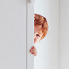 young boy peeking from behind cabinet