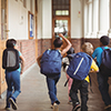 Rear view of happy pupils walking at corridor in school