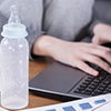 Close up of a woman working on laptop and baby bottle lying on table