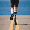 An athlete with a prosthetic leg running down the road towards the ocean.