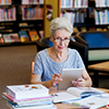 Elderly lady working with tablet and books in library
