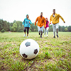 Friends running towards football in the countryside