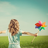 girl in green field with arms up holding multi-coloured fan