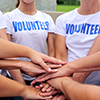 Group of people stacking hands wearing volunteer shirts