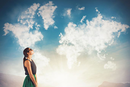 world map formed from clouds, woman gazing at sky