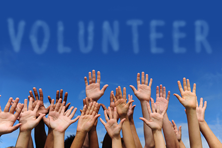 Volunteer written in cloudy text  over blue sky background. hands raised in air below words