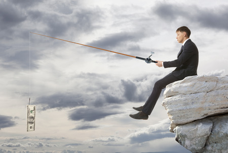 Young businessman sitting on top of rock and fishing
